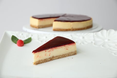Three sliced desserts on white plate: red berry cheesecake in foreground with green leaf and red berry garnish, and two round cakes in background