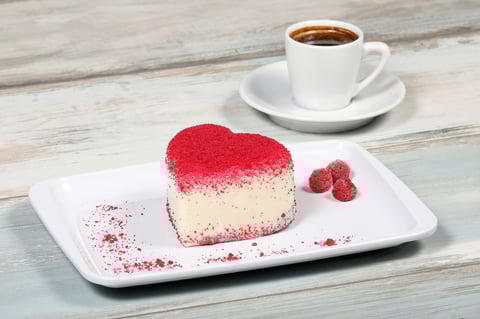 Heart-shaped dessert with red frosting and raspberries
